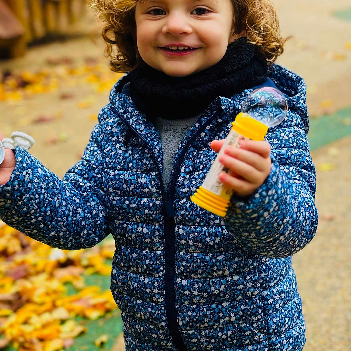 Alma a rejoint le concours — aidez-le/la à gagner de superbes lots ! autumn, blue_jacket, bubble, bubble_wand, child, curly_hair, daylight, fall, happy, jacket, leaves, nature, outdoor, path, person, playful, scarf, smiling, toy, young_child