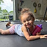 casual_clothing, child, curly_hair, daylight, face, floor, happy, home, indoor, person, pink_shorts, playful, relaxed, shoes, sippy_cup, smiling, toddler, toy, trampoline, white_tank_top