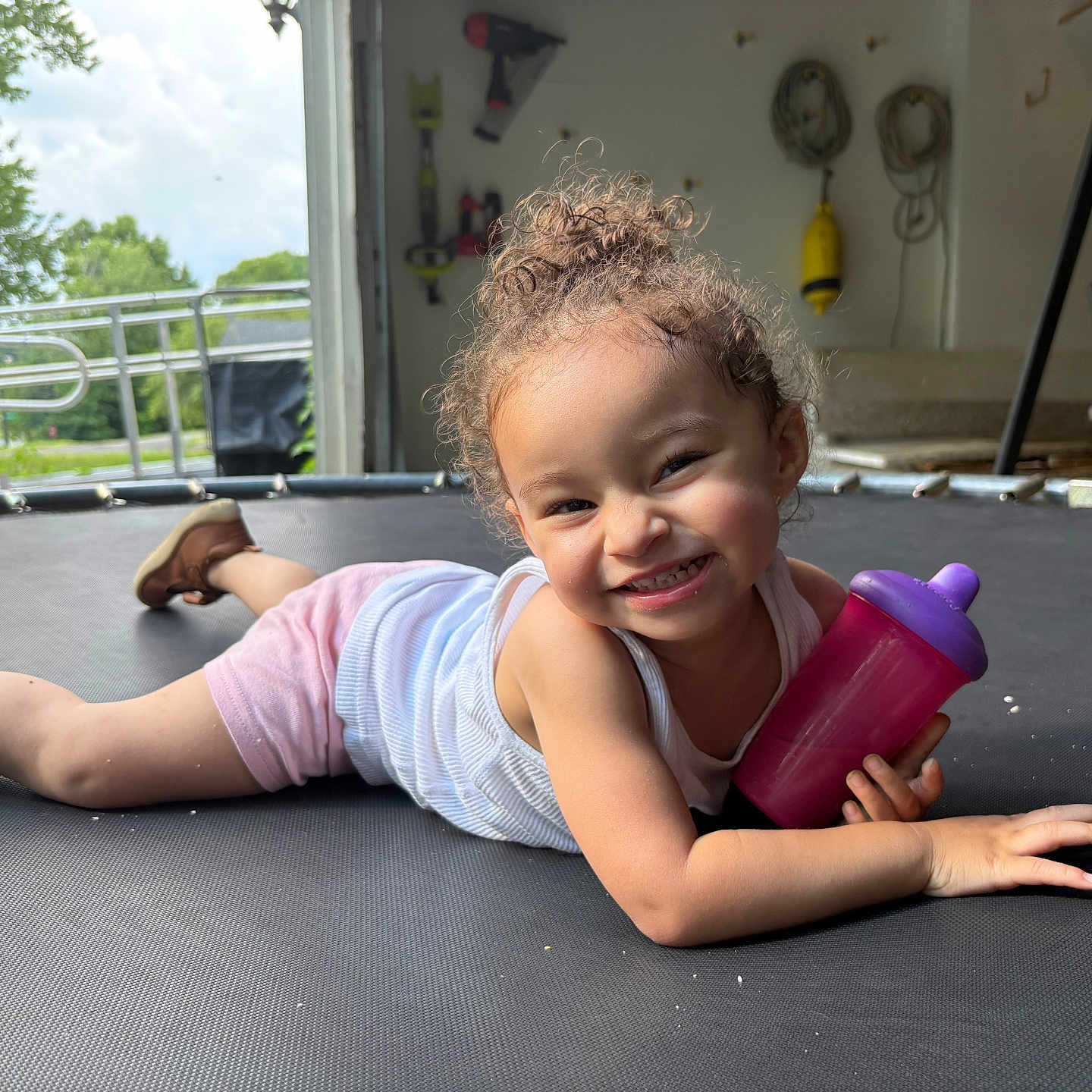 Amyalee joined the competition — help win amazing prizes! toddler, child, smiling, curly_hair, trampoline, sippy_cup, indoor, happy, playful, casual_clothing, pink_shorts, white_tank_top, shoes, face, person, floor, toy, home, daylight, relaxed