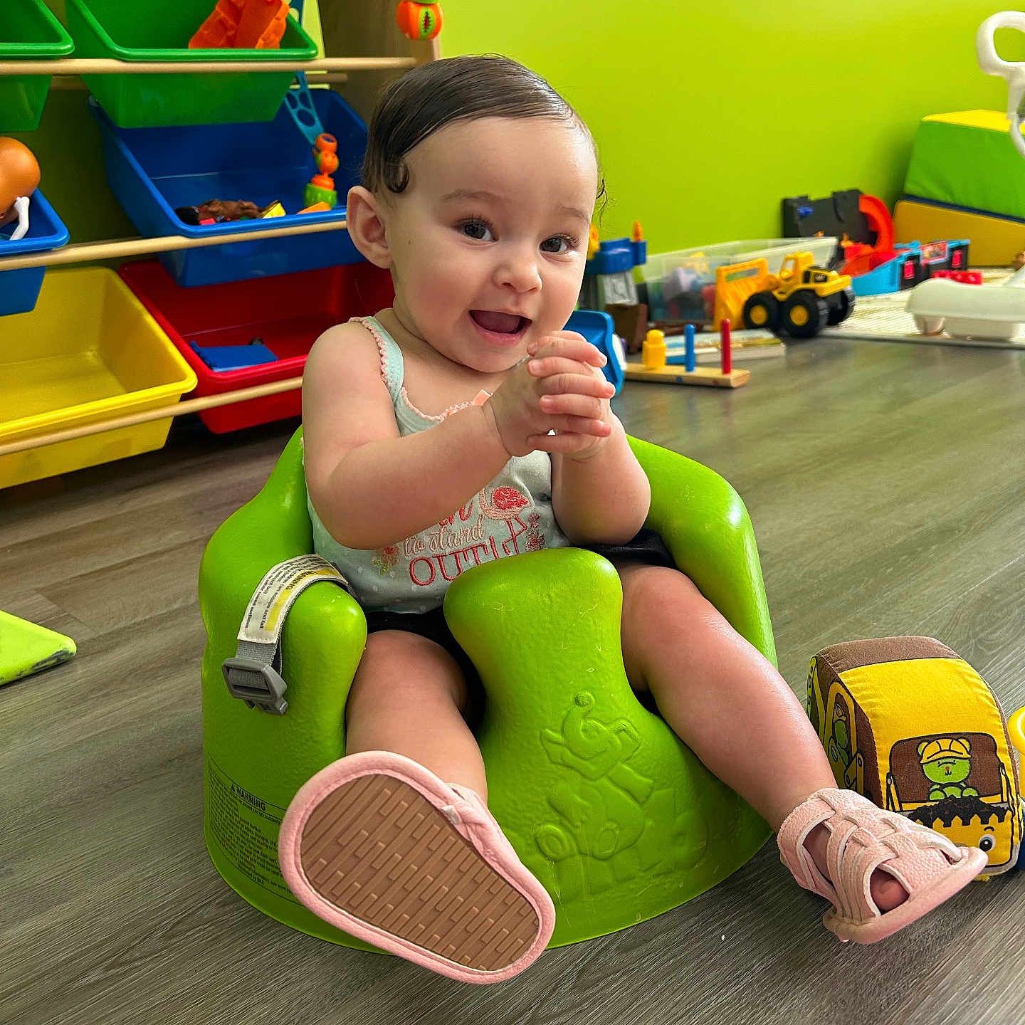 Amyalee joined the competition — help win amazing prizes! baby, casual_clothing, child, clapping, colorful_bins, cute, fabric_toy, floor, green_baby_seat, happy, indoor, infant, person, pink_shoes, plastic_toy, playroom, short_hair, smiling, toys, wooden_floor