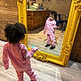 black_shoes, casual_clothing, chairs, child, curly_hair, floor, holding, indoor, looking, mirror, person, pink_tracksuit, reflection, room, shoes, spoon, table, tiled_wall, wooden_wall, yellow_frame