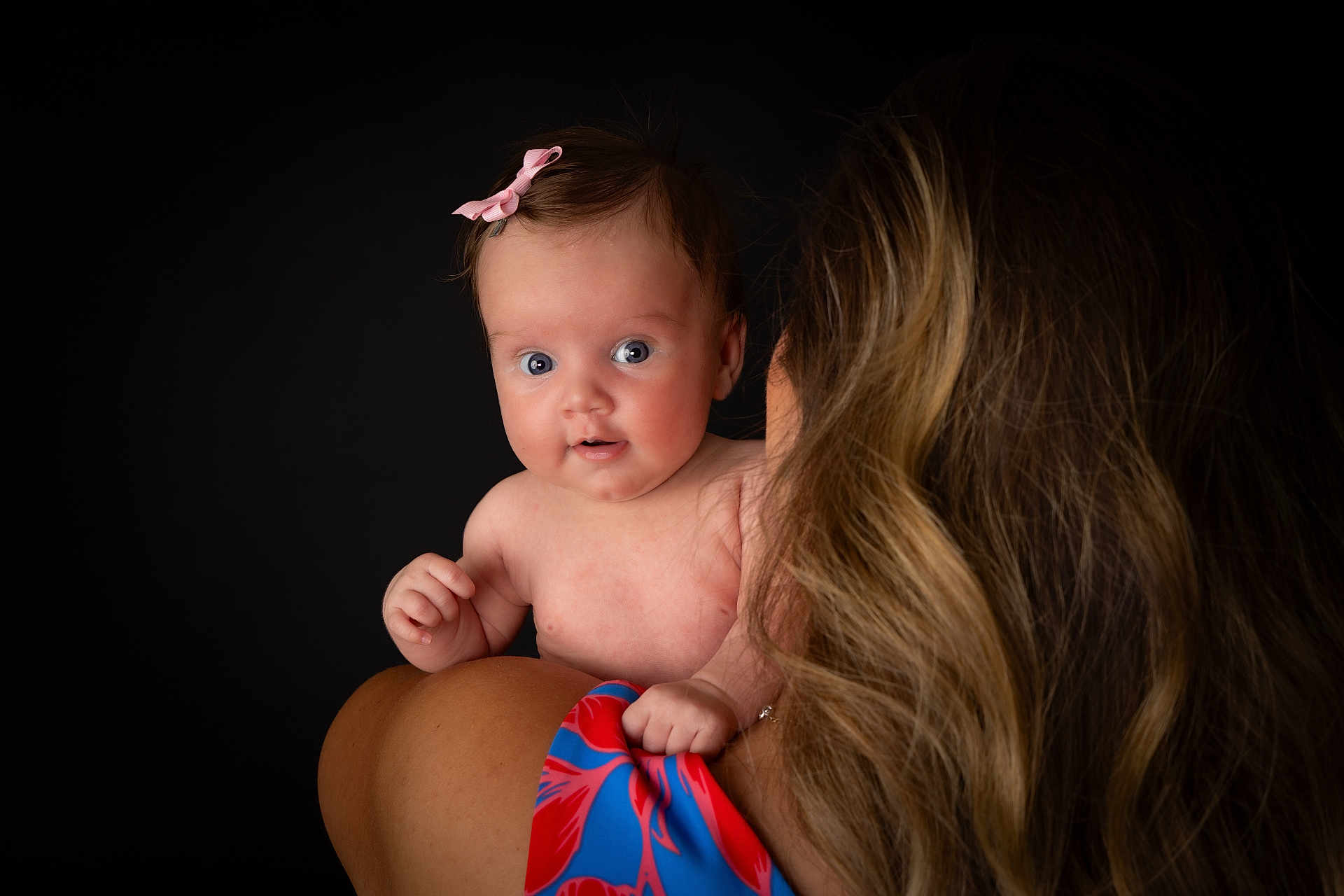 Esmé is registered to the contest to win money with this photo: baby, child, infant, person, shoulder, hair, pink_bow, blue_eyes, curious, portrait, studio, woman, adult, skin, closeup, expression, holding, colorful_clothing, back_view, head