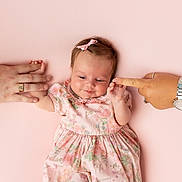 Esmé is registered to the contest to win money with this photo: baby, infant, pink, dress, bow, hands, adult_hands, floral_pattern, cute, child, portrait, holding_hands, watch, ring, skin, lying_down, soft_background, happy, family, togetherness