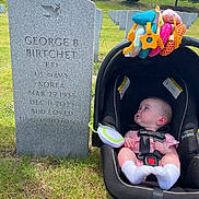 Riley joined the competition — help win amazing prizes! baby, car_seat, gravestone, cemetery, grass, toy, outdoor, trees, sunlight, infant, head, clothing, grass_field, memorial, military, nature, peaceful, portrait, person, seat