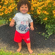 Julian joined the competition — help win amazing prizes! child, toddler, curly_hair, smiling, barefoot, grass, yellow_flowers, red_shorts, gray_tshirt, outdoor, garden, summer, holiday, 4th_of_july, nature, greenery, birdhouse, cute, happy, celebration