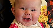 River is registered to the contest to win money with this photo: baby, bib, cheerful, child, close_up, cute, daisies, earring, face, happy, indoor, infant, person, pillow, pink_clothing, portrait, seated, smiling, sunflower, young