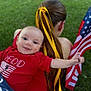 baby, child, person, red_shirt, yellow_ribbon, pony_tail, american_flag, grass, outdoor, smiling, happy, holding, portrait, casual_clothing, young_child, flag, nature, summer, toddler, celebration