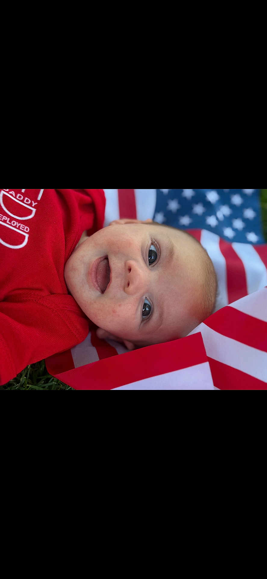 Barrett is registered to the contest to win money with this photo: baby, infant, face, smile, red_clothing, american_flag, patriotic, outdoor, grass, happy, portrait, cute, child, young, lying_down, closeup, skin, eye, expression, celebration