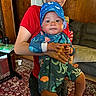 Kreedence is registered to the contest to win money with this photo: adult, baby, carpet, child, clothing, comfort, couch, face, hands, hat, holding, home, indoor, living_room, patterned_clothing, person, red_shirt, rug, smile, wood_paneling