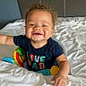 baby, bed, blanket, child, clothing, curly_hair, cute, furniture, happy, home, indoor, infant, joy, person, playful, reaching, shirt, smiling, toddler, toy