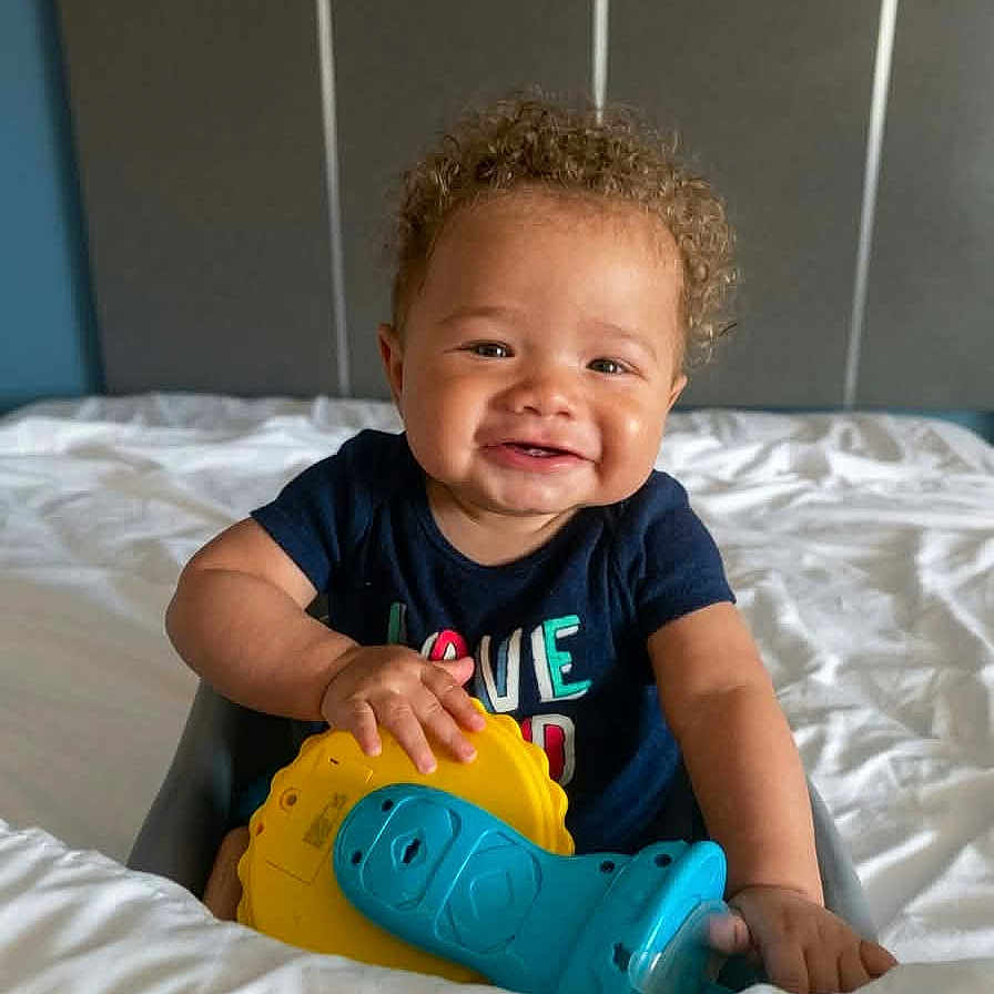 Kreedence is registered to the contest to win money with this photo: baby, bed, bedroom, blue_toy, chair, child, clothing, curly_hair, cute, happy, indoor, infant, person, play, portrait, smile, toddler, toy, yellow_toy, young_child