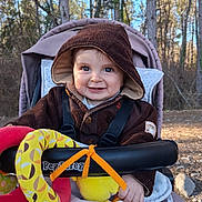 Charly a rejoint le concours — aidez-le/la à gagner de superbes lots ! baby, cheeks, cozy, eyes, forest, happy, hooded_jacket, infant, nature, outdoors, plush_toy, portrait, ring_toy, seat_harness, smile, stroller, sunlight, toys, trees, woodland