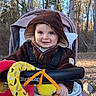 baby, cheeks, cozy, eyes, forest, happy, hooded_jacket, infant, nature, outdoors, plush_toy, portrait, ring_toy, seat_harness, smile, stroller, sunlight, toys, trees, woodland