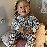 Alba Rosa participe au concours pour gagner de l'argent avec cette photo : toddler, child, smile, happy, indoor, cushion, heart_pattern, clothing, headband, bottle, floor, wooden_floor, furniture, person, portrait, sitting, cute, young_child, baby_shoes, long_sleeves