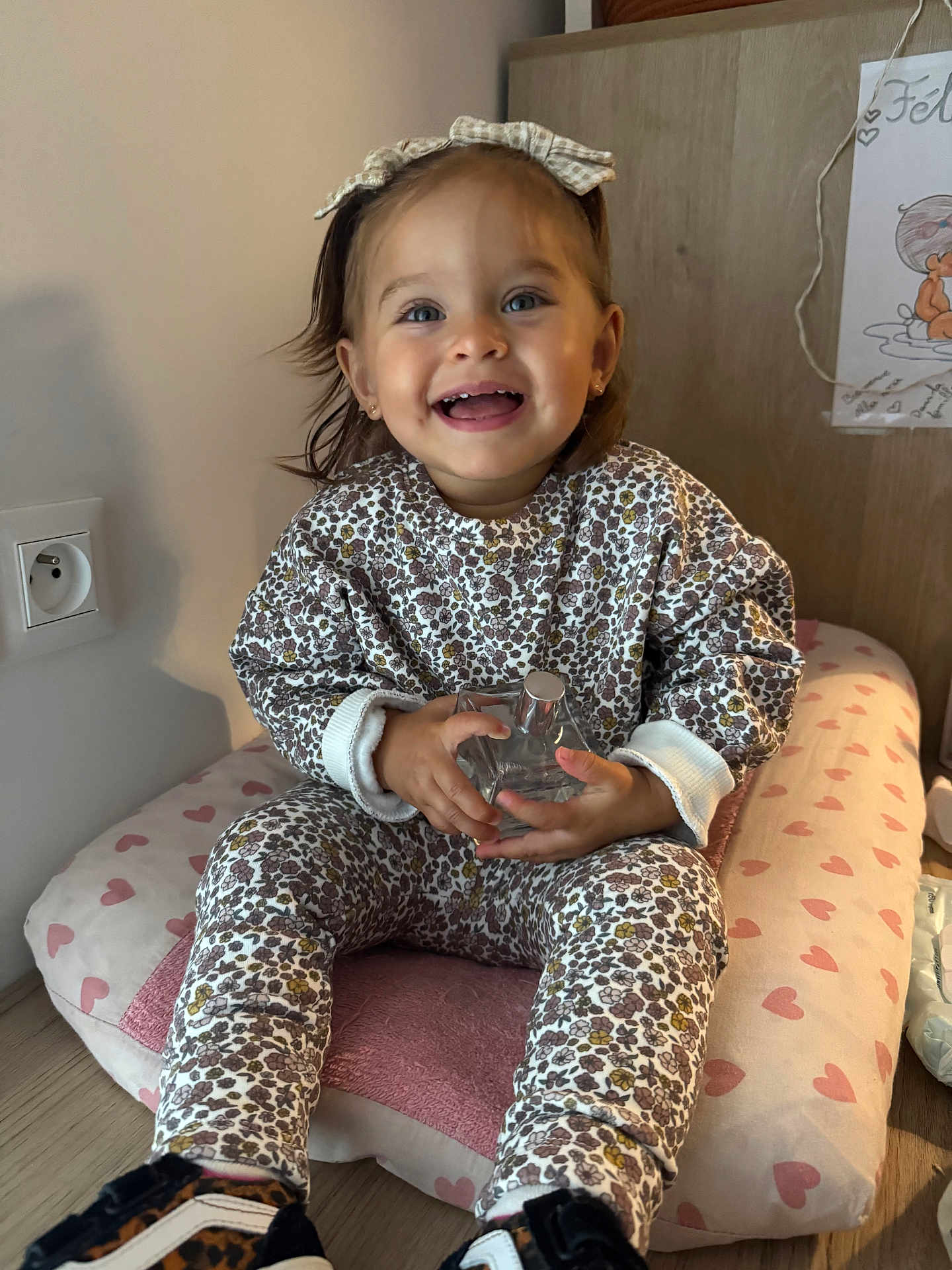 Alba Rosa participe au concours pour gagner de l'argent avec cette photo : toddler, child, smile, happy, indoor, cushion, heart_pattern, clothing, headband, bottle, floor, wooden_floor, furniture, person, portrait, sitting, cute, young_child, baby_shoes, long_sleeves