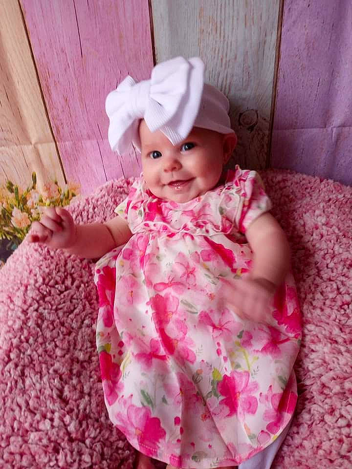 Octavia is registered to the contest to win money with this photo: arm, baby, baby_laughing, baby_toddler_clothing, child, comfort, dress, eye, face, happy, hat, head, headwear, joy, magenta, pattern, person, petal, pink, purple