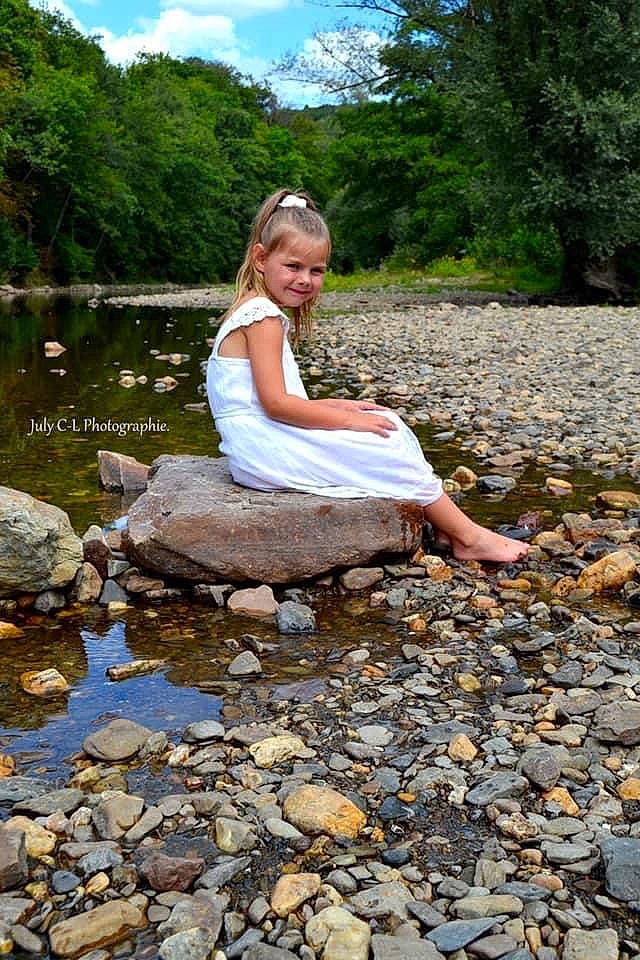 Enola participe au concours pour gagner de l'argent avec cette photo : bank, bedrock, botany, dress, forest, grass, happy, joy, landscape, leisure, natural_environment, natural_landscape, people_in_nature, person, plant, sky, stream, summer, tree, water
