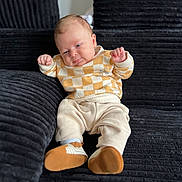 Inacio a rejoint le concours — aidez-le/la à gagner de superbes lots ! baby, black_couch, child, clothing, corduroy, couch, cozy, expression, face, feet, hands, indoors, infant, pants, portrait, relaxed, seated, shoes, soft_lighting, sweater
