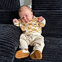 baby, black_couch, child, clothing, corduroy, couch, cozy, expression, face, feet, hands, indoors, infant, pants, portrait, relaxed, seated, shoes, soft_lighting, sweater