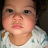 Carter is registered to the contest to win money with this photo: baby, child, closeup, curly_hair, cute, dinosaur_print, expression, eyebrows, face, head, human, indoors, looking_at_camera, person, portrait, serious_expression, shirt, skin, toddler, young_child