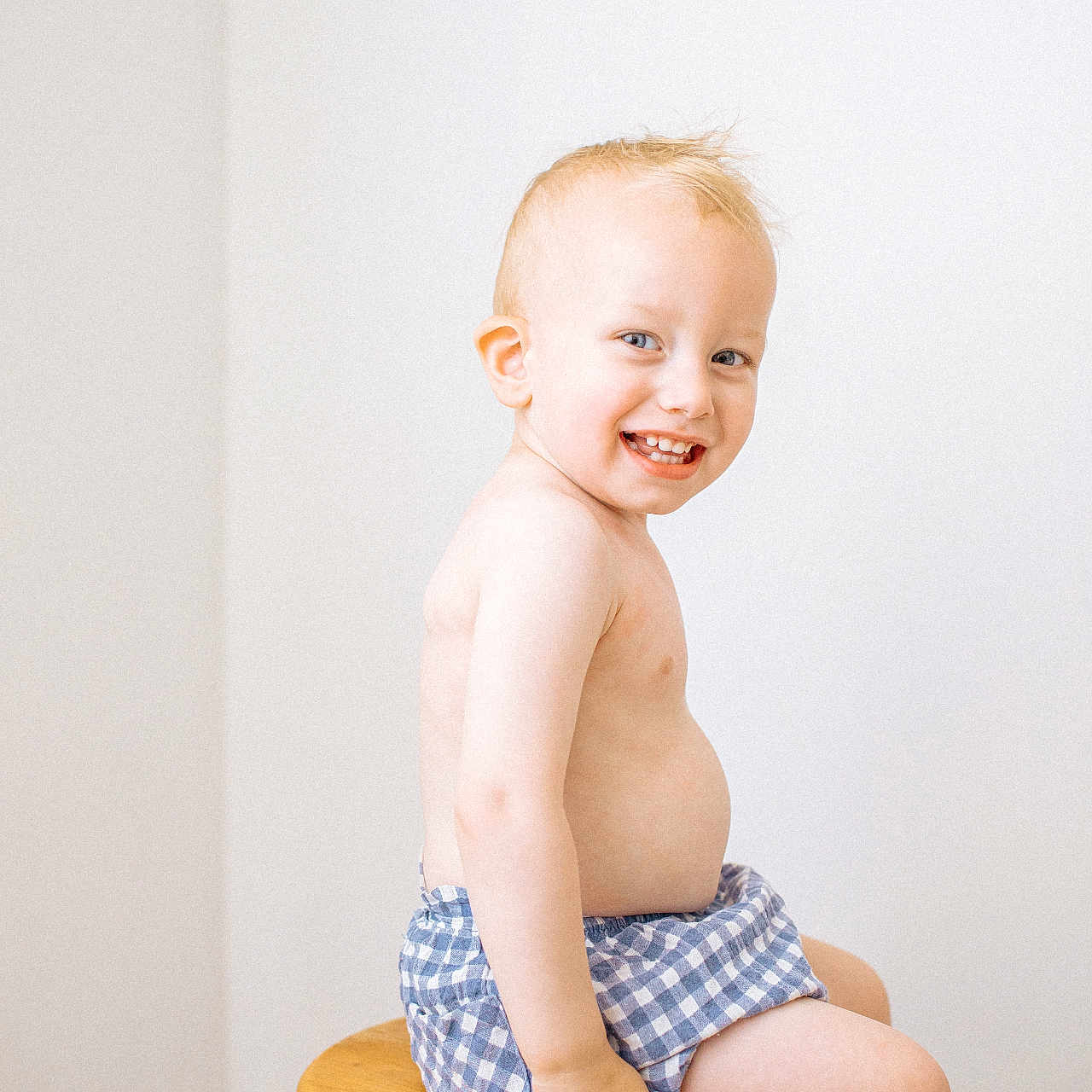 Lip participe au concours pour gagner de l'argent avec cette photo : bare_chest, blond_hair, blue_shorts, checkered, child, cute, happy, indoor, innocence, person, playful, portrait, sitting, skin, smiling, stool, toddler, white_wall, wooden_furniture, young_child