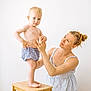 Lip a rejoint le concours — aidez-le/la à gagner de superbes lots ! toddler, child, woman, adult, standing, stool, holding_hands, blue_shorts, light_skin, blonde_hair, tattoo, indoor, minimalist_background, casual_clothing, mother_and_child, portrait, barefoot, gentle_touch, affection, family