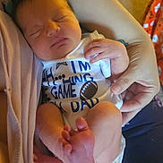 Everlee is registered to the contest to win money with this photo: newborn, baby, sleeping, infant, onesie, football, text, hand, foot, person, holding, close_up, cute, peaceful, skin, clothing, indoor, human, sleep, rest