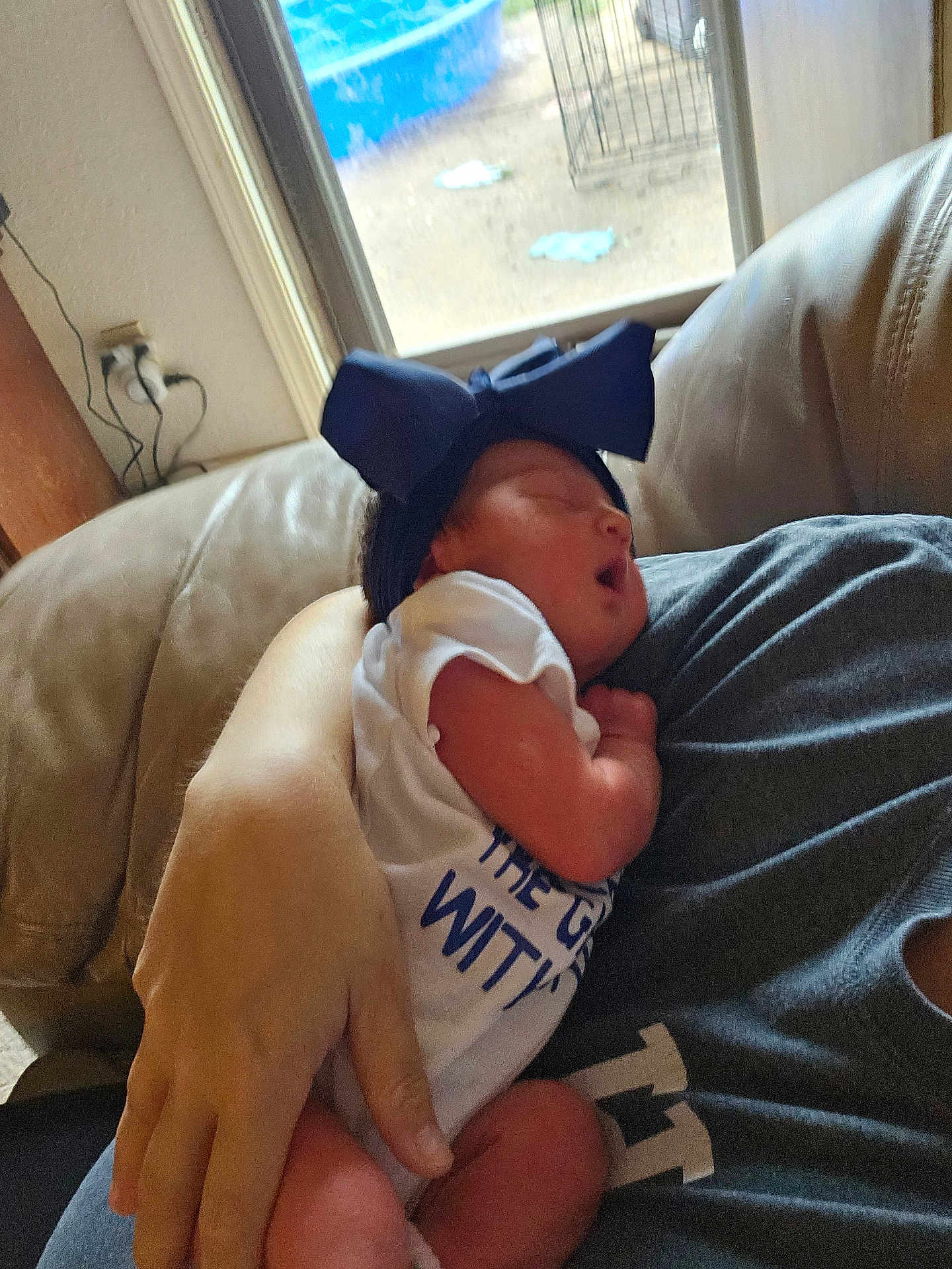 Everlee is registered to the contest to win money with this photo: baby, newborn, sleeping, headband, bow, person, hand, arm, couch, indoor, window, clothing, white_shirt, skin, comfort, rest, infant, holding, blurred_background, casual