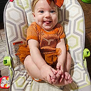 Everlee is registered to the contest to win money with this photo: baby, infant, child, orange_outfit, headband, bow, smile, tongue_out, baby_seat, patterned_cushion, happy, cute, hands, feet, wooden_floor, toy, playtime, indoors, cheerful, closeup