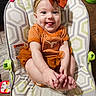 baby, infant, child, orange_outfit, headband, bow, smile, tongue_out, baby_seat, patterned_cushion, happy, cute, hands, feet, wooden_floor, toy, playtime, indoors, cheerful, closeup