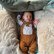 Baptiste a rejoint le concours — aidez-le/la à gagner de superbes lots ! baby, sleeping, brown_overalls, boots, pillows, blankets, cozy, infant, soft_texture, resting, cute, child, indoors, comfortable, peaceful, clothing, portrait, warm, nursery, relaxing