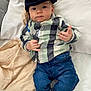 baby, child, infant, plaid_shirt, cap, jeans, socks, blanket, bed, pacifier, cute, lying_down, indoor, person, fashion, smiling, headwear, clothing, hands, portrait