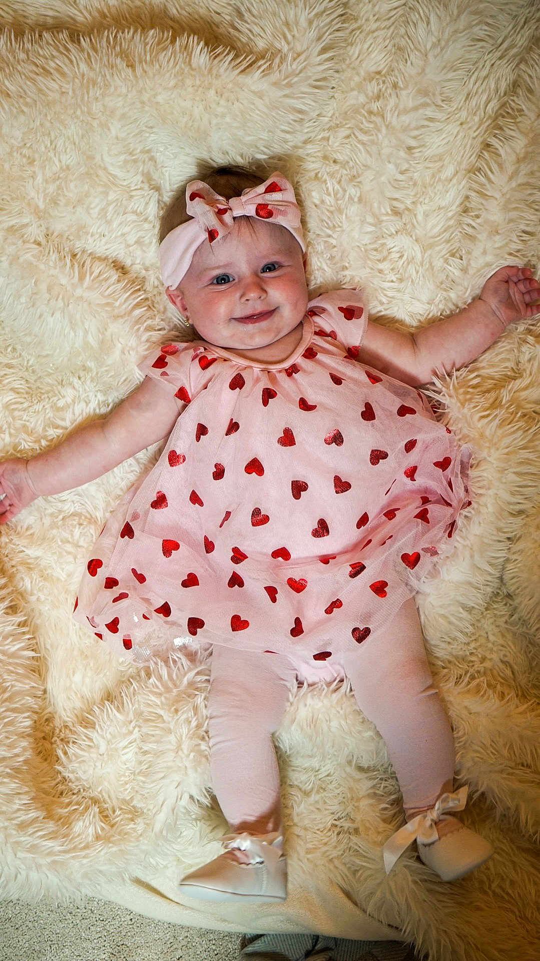 Autumn-Rose is registered to the contest to win money with this photo: baby, infant, pink_dress, headband, bow, red_hearts, leggings, white_shoes, smiling, cute, fluffy_rug, soft_texture, lying_down, child, adorable, portrait, happy, indoors, clothing, baby_fashion