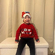 Noé participe au concours pour gagner de l'argent avec cette photo : child, toddler, smile, red_sweater, winter_hat, striped_socks, black_pants, indoor, bench, curtain, happy, festive, holiday, portrait, sitting, clothing, cute, person, cozy, background