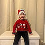 Noé participe au concours pour gagner de l'argent avec cette photo : background, bench, black_pants, child, clothing, cozy, curtain, cute, festive, happy, holiday, indoor, person, portrait, red_sweater, sitting, smile, striped_socks, toddler, winter_hat