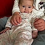 baby, child, infant, person, hands, onesie, clothing, couch, red_couch, seated, comfort, indoor, cute, face, blue_eyes, expression, holding, sitting, casual, cozy
