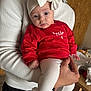 adult, baby, bow, child, clothing, cozy, curious, cute, furniture, hand, headband, holding, indoor, infant, leggings, person, portrait, red_sweater, table, white_sweater