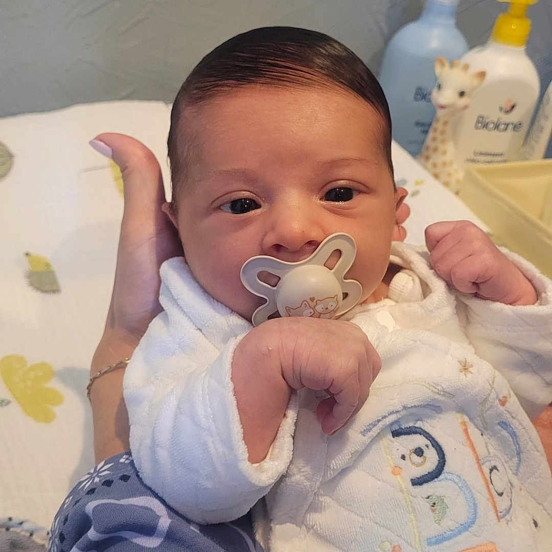 Andréa a rejoint le concours — aidez-le/la à gagner de superbes lots ! baby, infant, pacifier, onesie, hand, person, face, cute, newborn, baby_lotion, toy, giraffe_toy, bed, blanket, sleepwear, child, skin, head, expression, comfort