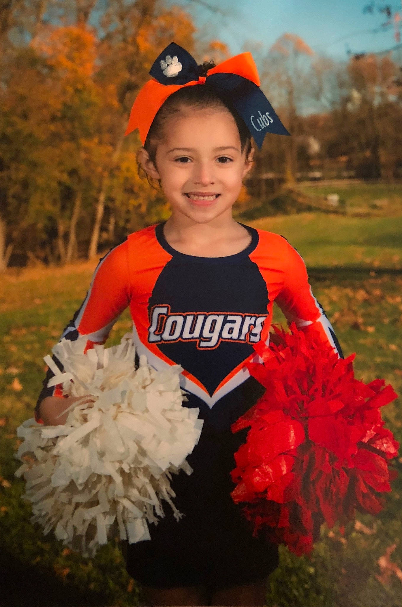 Emmaleigh is registered to the contest to win money with this photo: american_football, cheering, cheerleading, cheerleading_uniform, child, clothing, competition_event, costume, costume_accessory, happy, joy, person, pom_pom, smile, sports_uniform, sportswear, team_sport, toddler, uniform