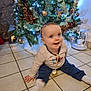 Jules participe au concours pour gagner de l'argent avec cette photo : baby, celebration, child, christmas_tree, cozy_clothing, cute, decorations, festive, happy, holiday, home, indoor, infant, lights, ornaments, pacifier, sitting, smiling, tiled_floor, winter