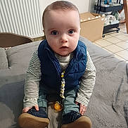 Jules a rejoint le concours — aidez-le/la à gagner de superbes lots ! baby, child, infant, blue_eyes, striped_shirt, navy_vest, pacifier, indoor, home, blanket, floor_tiles, radiator, sitting, shoes, cute, person, furniture, toy, expression, clothing