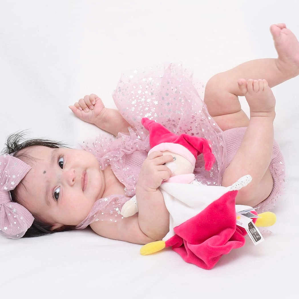 Trida participe au concours pour gagner de l'argent avec cette photo : adorable, baby, bare_feet, child, curly_hair, cute, indoor, infant, jester_doll, lying_down, pink_bow, playful, plush_toy, portrait, small_hands, smiling, soft_texture, sparkly_clothing, white_background, young