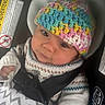 baby, child, car_seat, knitted_hat, colorful, sweater, blanket, safety, seatbelt, infant, cute, portrait, indoors, warm_clothing, young_child, closeup, person, face, headwear, comfort