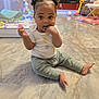 baby, child, indoor, floor, marble_floor, sitting, toys, playpen, person, curly_hair, double_buns, casual_clothing, pants, tshirt, hand_in_mouth, bright, home, cute, curious, young_child