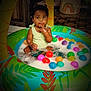 toddler, child, inflatable_pool, foam, plastic_balls, colorful, indoor, curious, play, water, green, yellow, red, blue, pink, orange, person, baby, sitting, cute