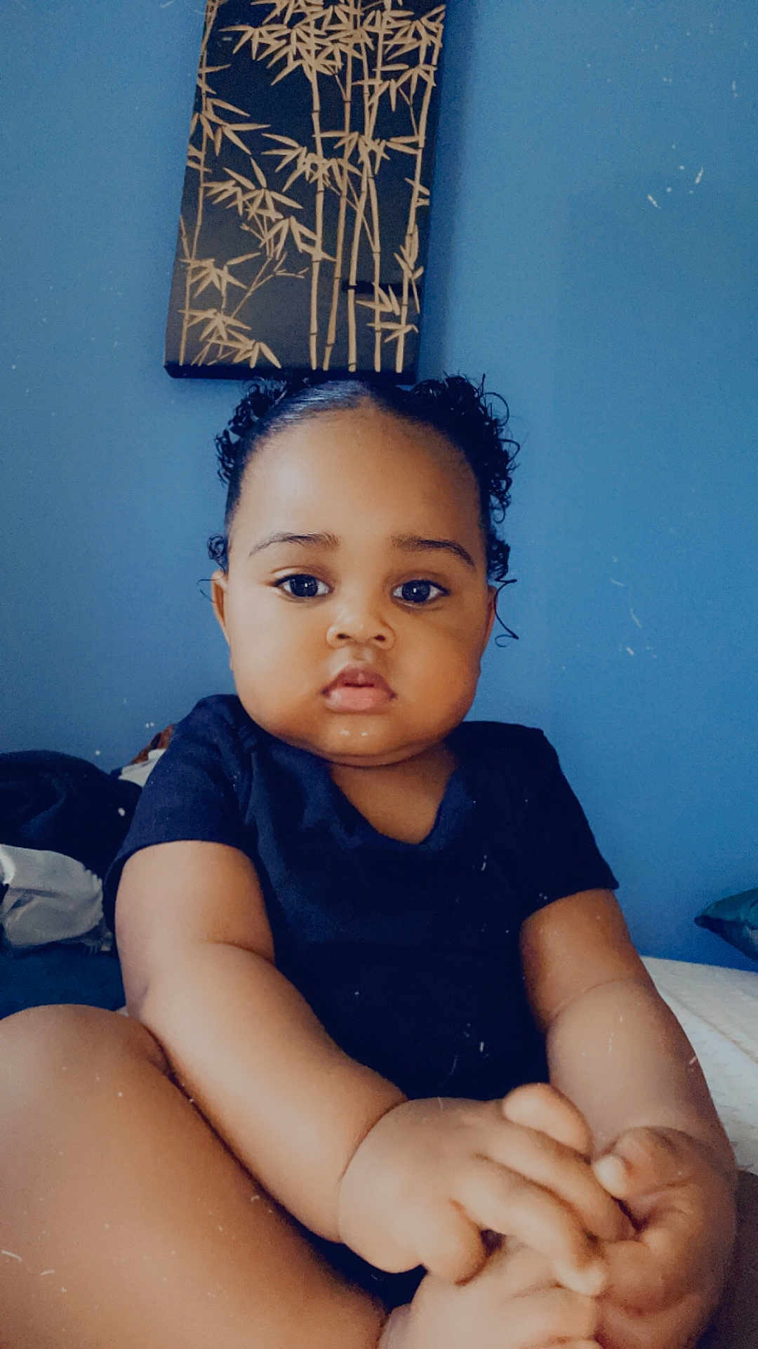 Julie Kay is registered to the contest to win money with this photo: baby, child, infant, pigtails, blue_wall, bamboo_artwork, hands, toes, curious, indoors, portrait, cute, furniture, clothing, black_shirt, sitting, skin, face, person, young