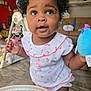 baby, child, indoor, curly_hair, toy, clothing, face, person, floor, furniture, living_room, couch, plaything, cute, expression, infant, home, smiling, holding, curiosity