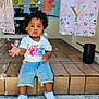 toddler, child, bubbles, curly_hair, sitting, outdoor, birthday, banner, cartoon, bus, pig, cat, balloon, concrete, tiles, shoes, shorts, shirt, celebration, party