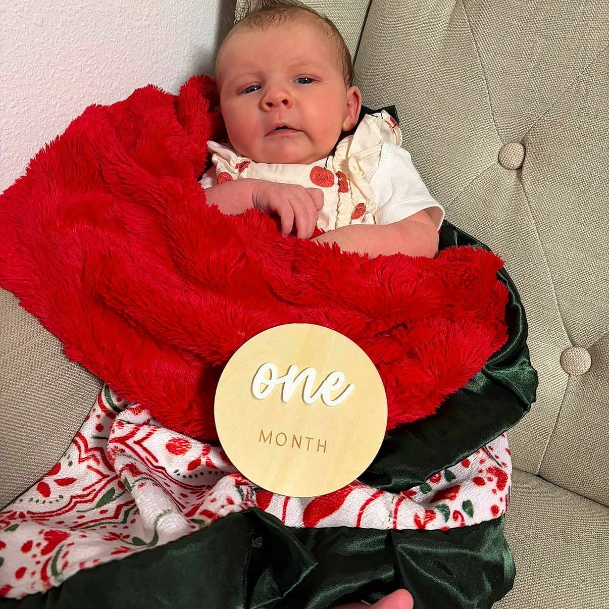 Grace is registered to the contest to win money with this photo: baby, infant, blanket, red_blanket, green_satin, wooden_sign, one_month, milestone, chair, tufted_chair, foot, bare_foot, festive, holiday, patterned_blanket, face, person, cute, portrait, indoors