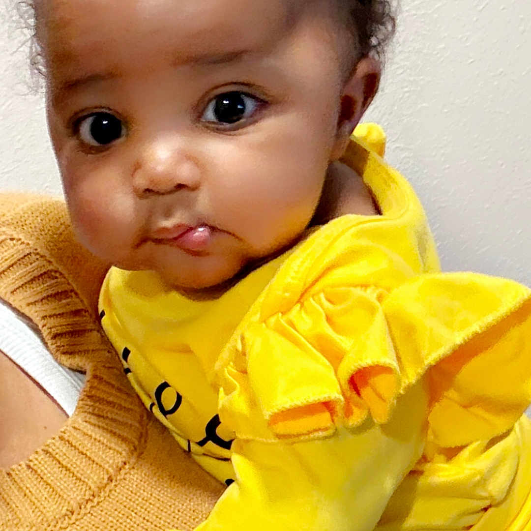 Tatiana is registered to the contest to win money with this photo: baby, child, yellow_clothing, bow, curly_hair, big_eyes, cute, infant, portrait, person, hand, knitted_sweater, holding, indoor, skin, face, expression, young_child, warm_colors, adorable